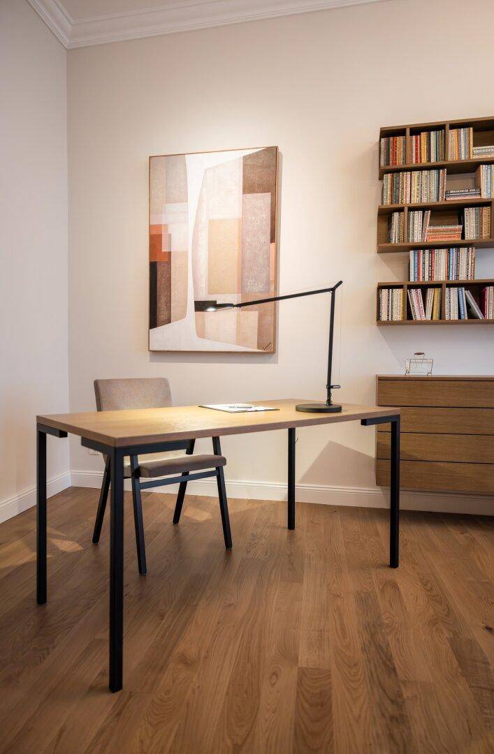 Moderner Schreibtisch mit minimalistischer Lampe und abstrakter Kunst in einem hellen Arbeitszimmer.