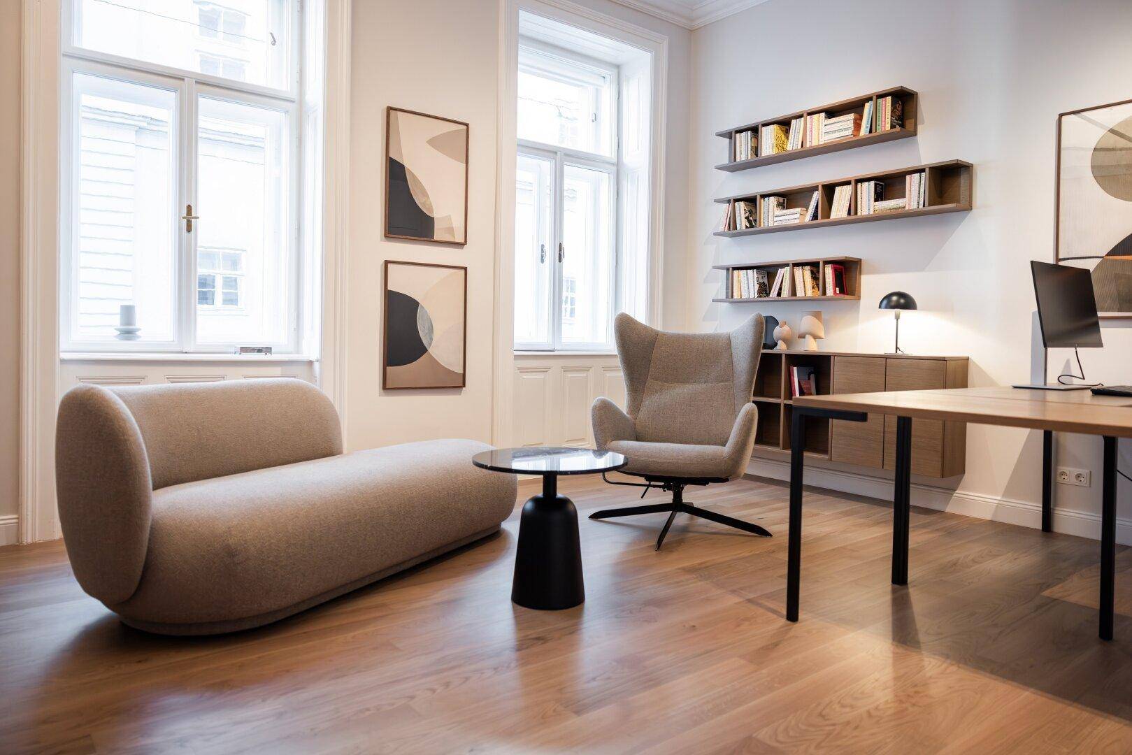 Helles Büro mit bequemer Sitzgelegenheit, Schreibtisch, Bücherregalen und großen Fenstern.