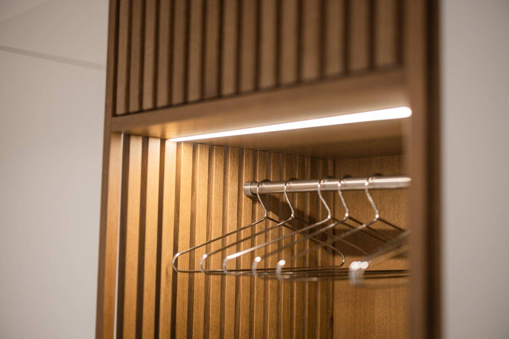 Detailansicht einer integrierten Garderobe mit Kleiderbügeln, umgeben von eleganten Holzlamellen.