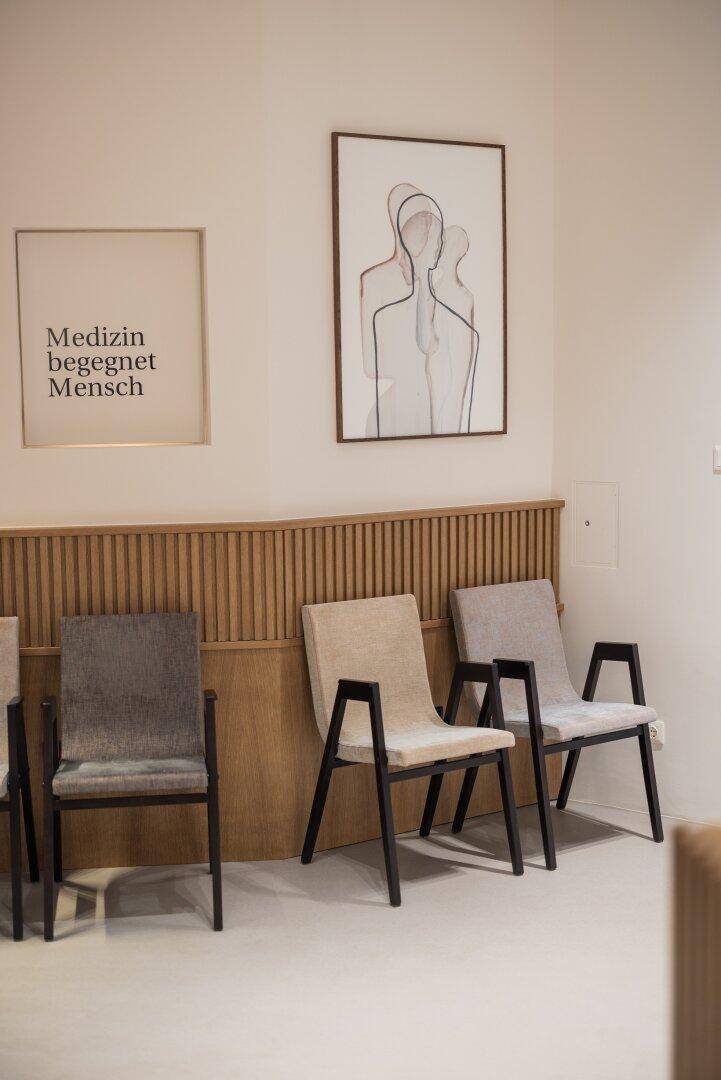 Wartebereich mit bequemen Stühlen und Holzlamellenverkleidung, ergänzt durch moderne Kunstwerke.