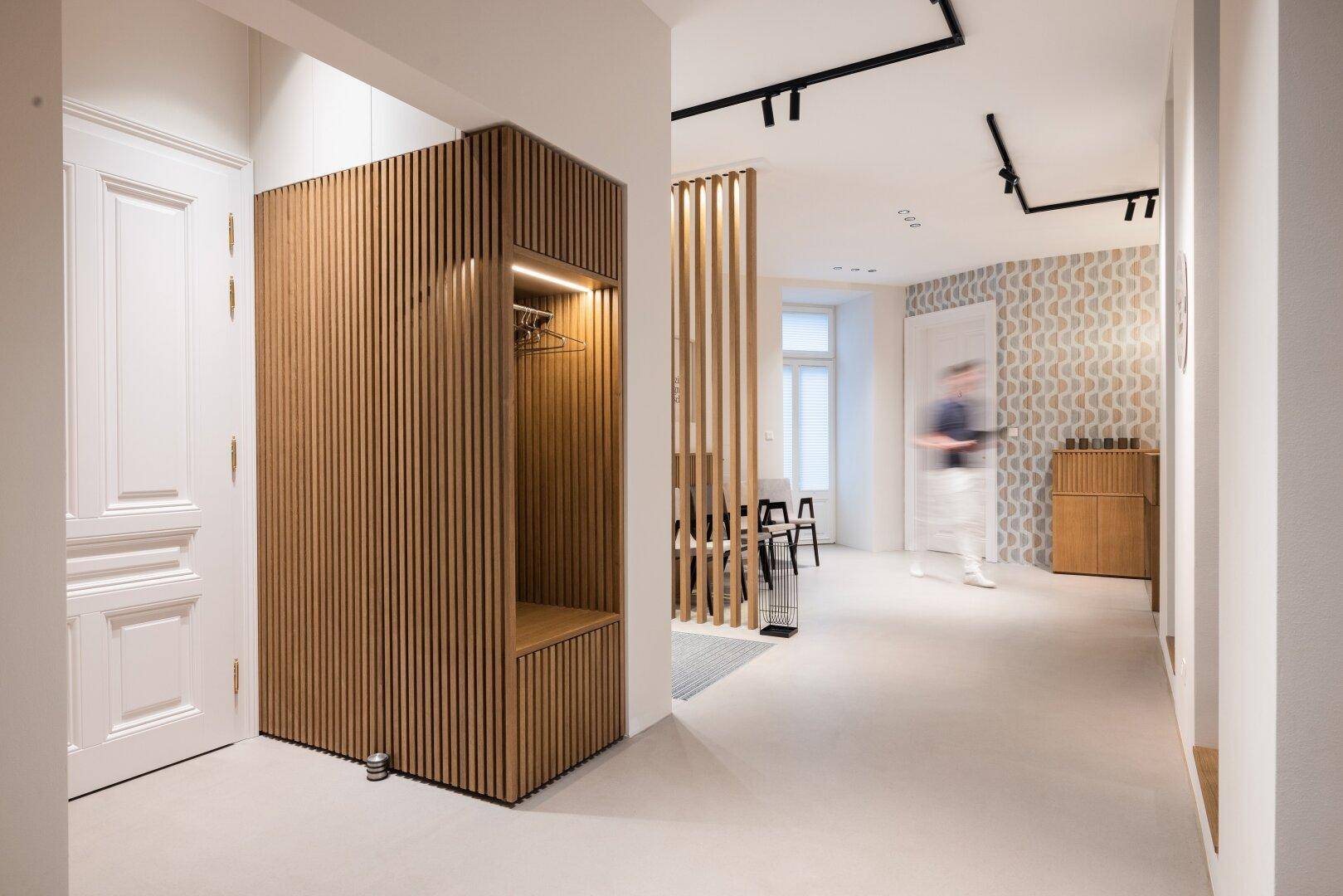Heller Eingangsbereich mit Holzlamellenverkleidung, integrierter Garderobe und moderner Beleuchtung.