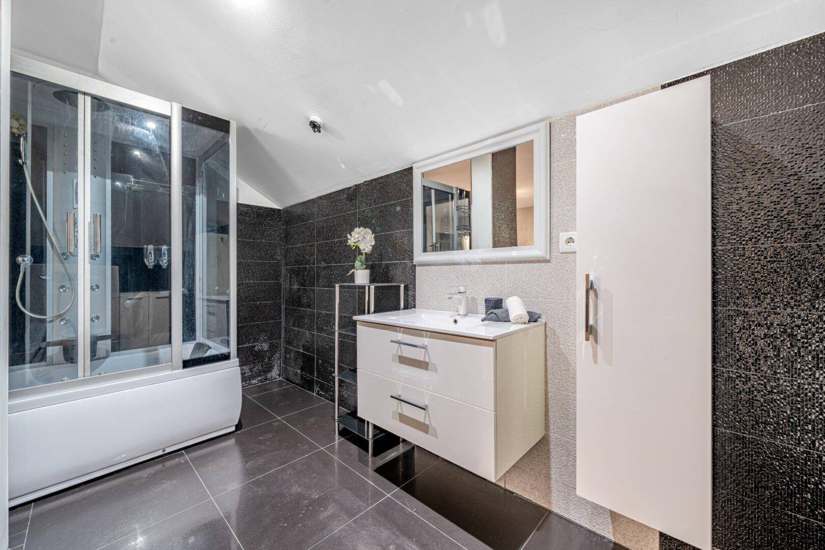 Modernes Badezimmer mit Duschkabine, Waschbecken und dunklen Fliesen.