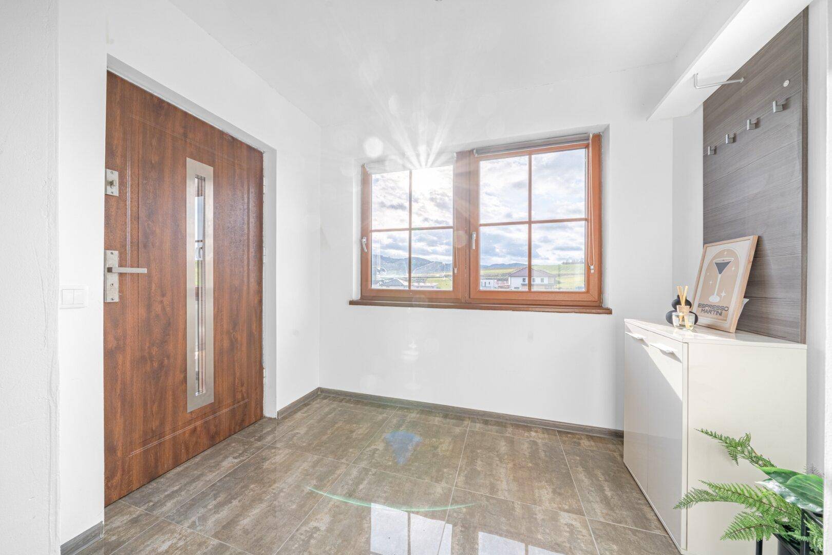 Heller Eingangsbereich mit Fliesenboden, Holztür und Fenster mit Weitblick.