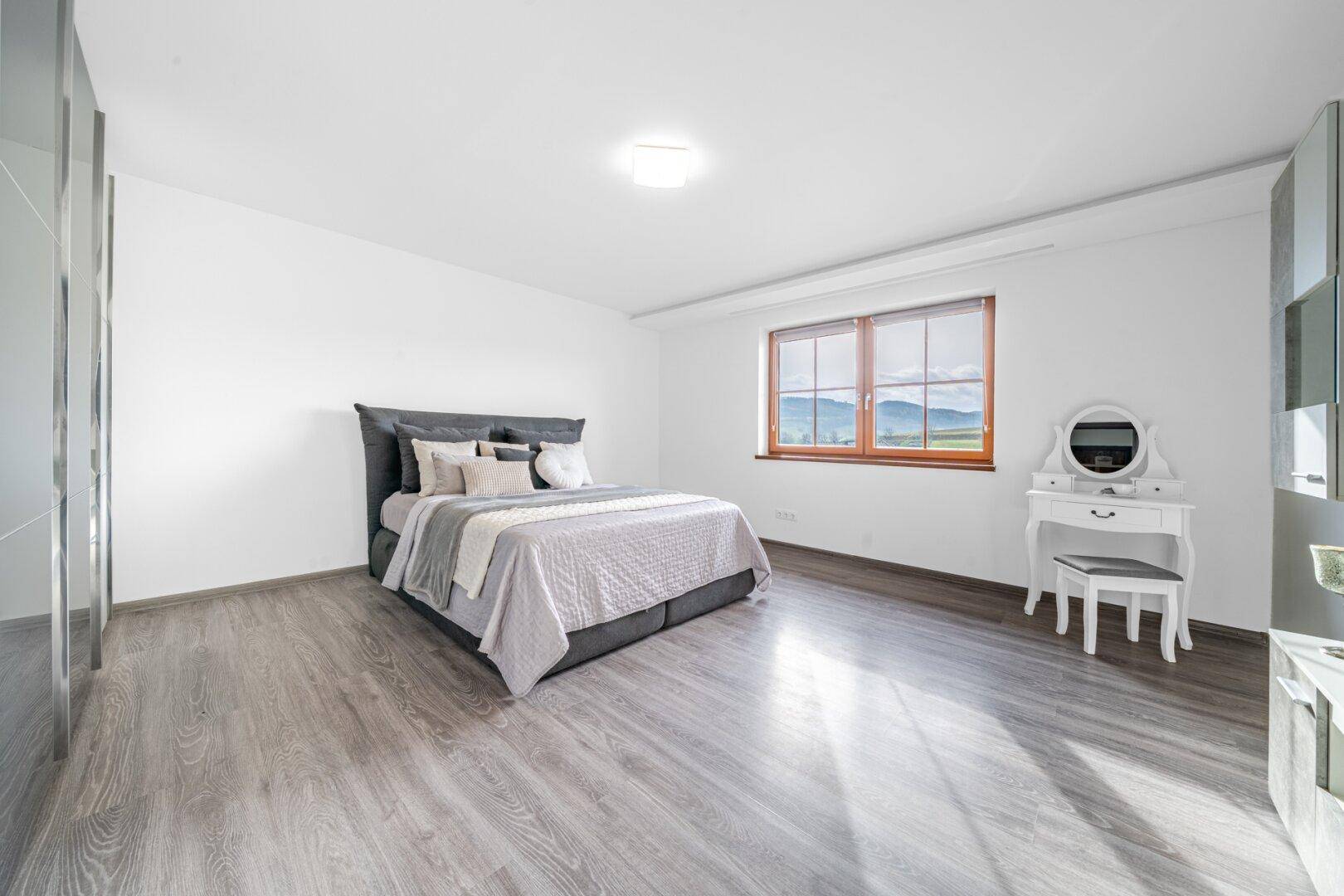 Helles Schlafzimmer mit Holzboden, großem Fenster und Bergblick.