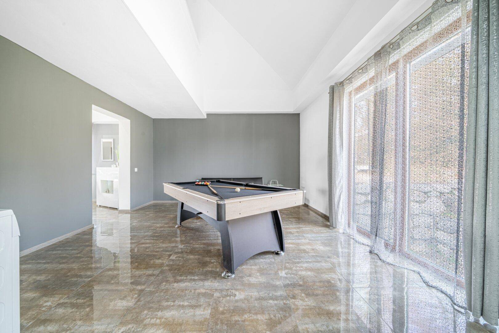 Geräumiger Spielzimmer mit Billardtisch, großen Fenstern und glänzenden Fliesen.