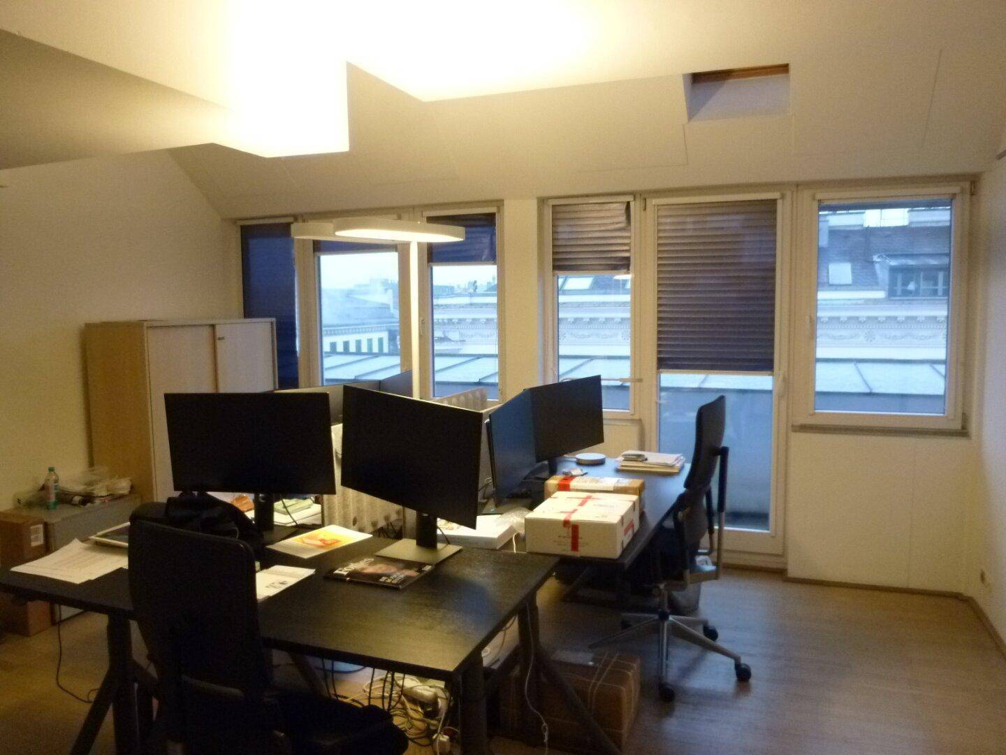 Geräumiges Büro mit mehreren Arbeitsplätzen, großen Fenstern und Blick auf die Dächer der Stadt.