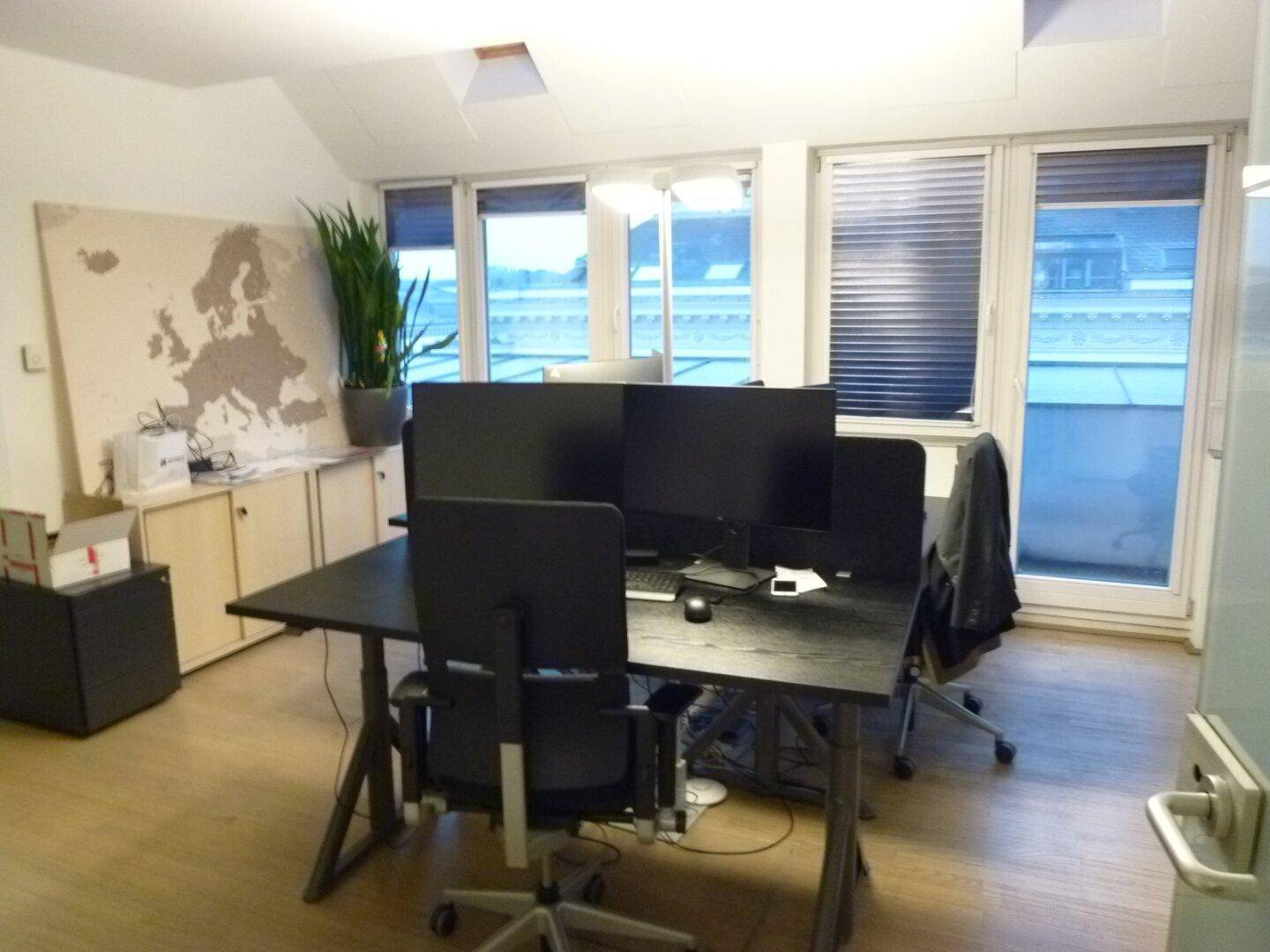 Helles Büro mit mehreren Arbeitsplätzen, großen Fenstern und Blick auf die umliegenden Gebäude.