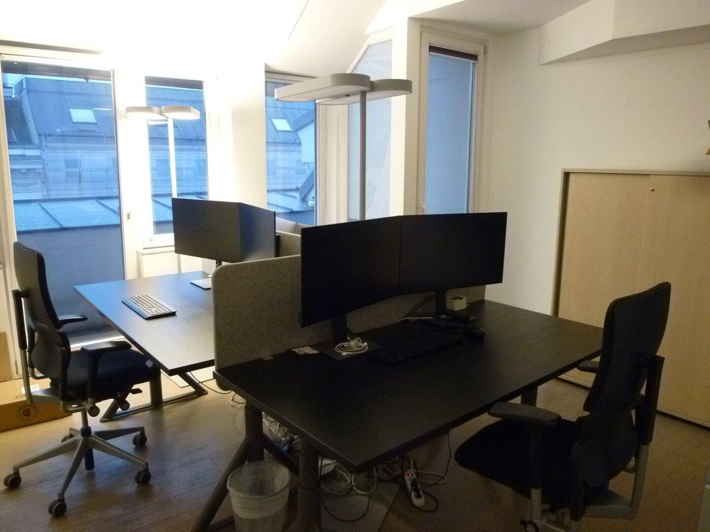 Helles Büro mit zwei modernen Arbeitsplätzen, großen Fenstern und Blick auf die Dächer.