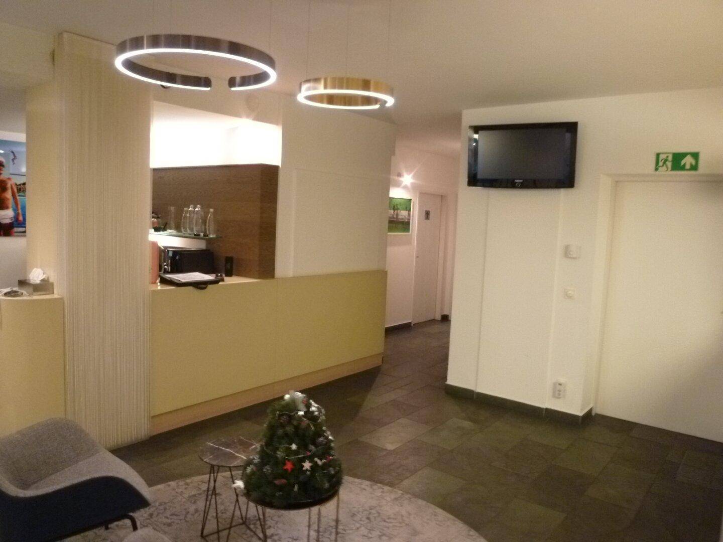 Empfangsbereich mit modernen Hängeleuchten, einem Fernseher und einem kleinen Weihnachtsbaum.
