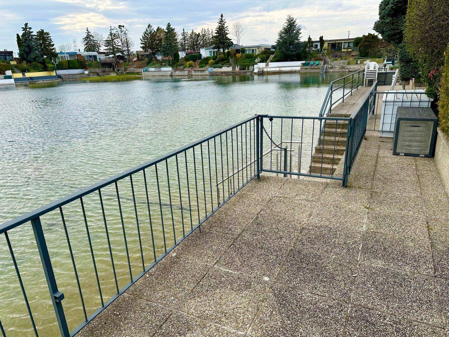 Gepflasterte Terrasse mit Geländer und direktem Zugang zum See, umgeben von weiteren Häusern.