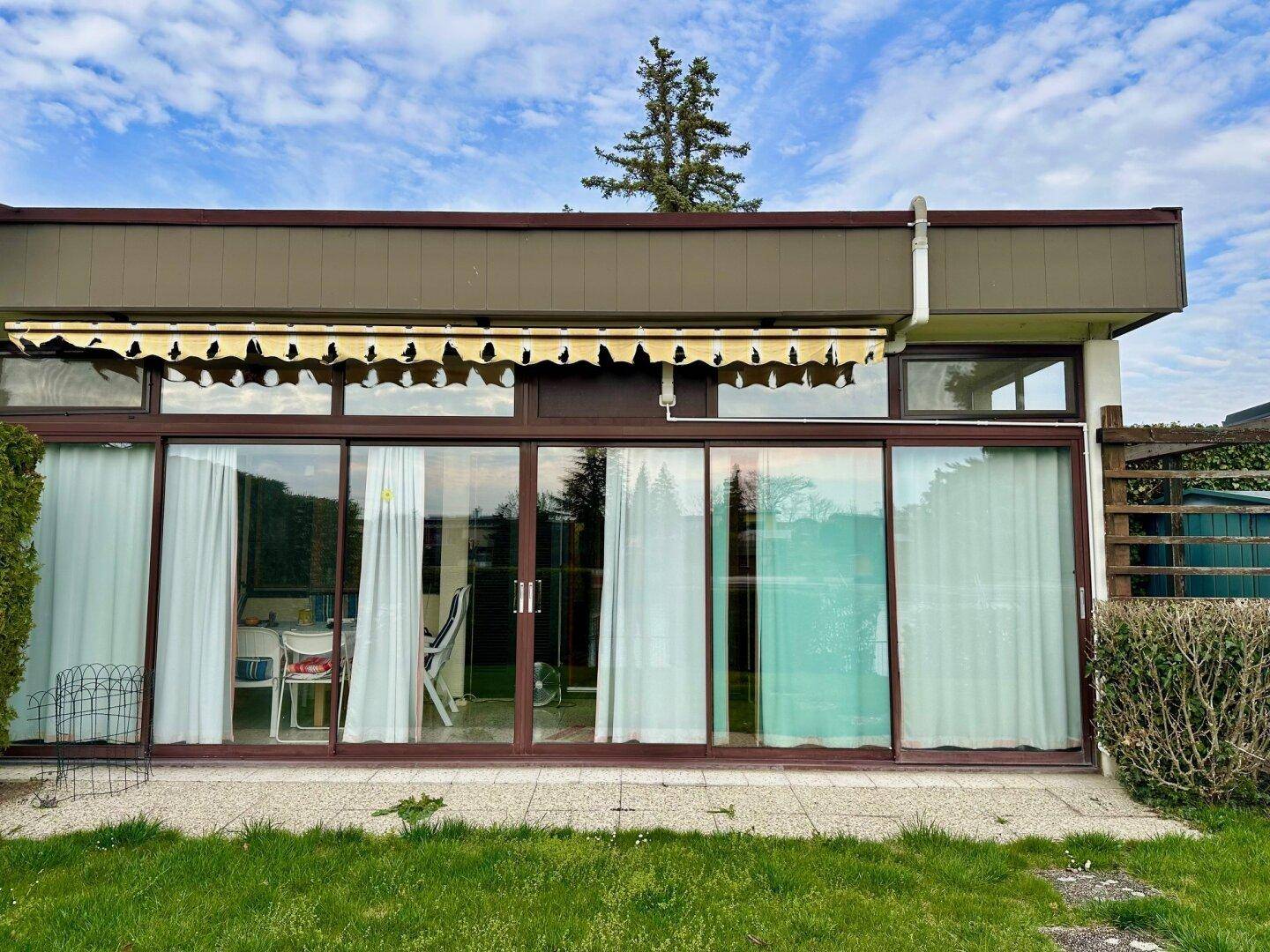 Rückansicht des Hauses mit großer Fensterfront, Markise und gepflegtem Rasenbereich.