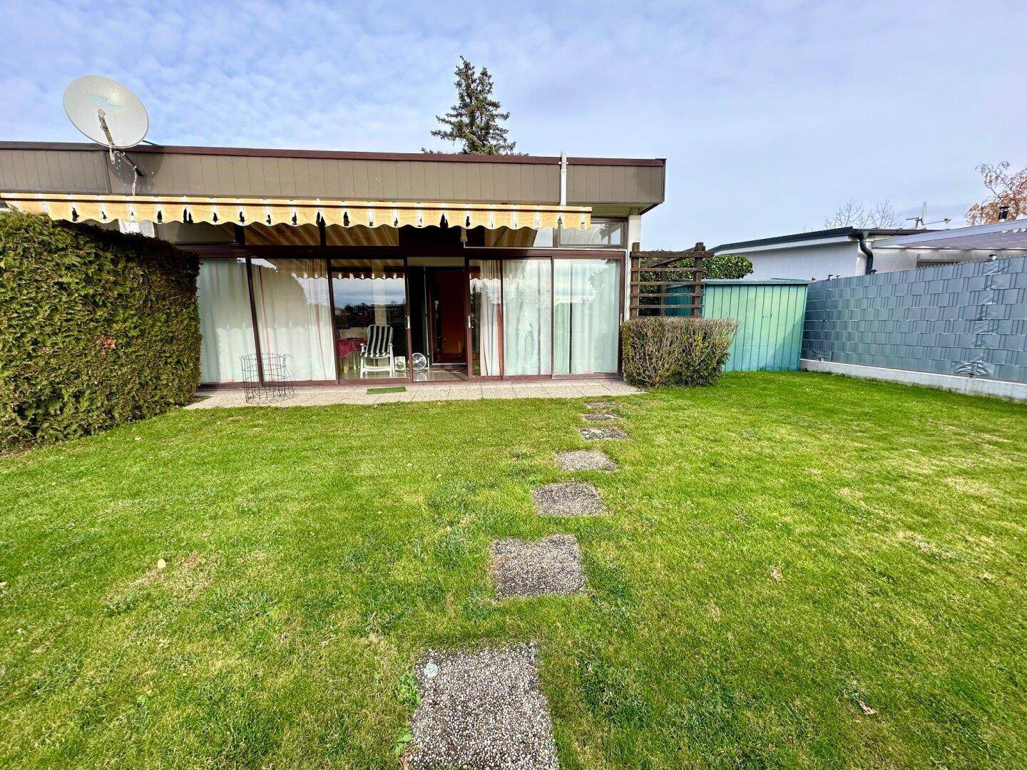 Gepflegter Gartenbereich mit Rasen, Steinplattenweg und Zugang zur verglasten Hausfassade.