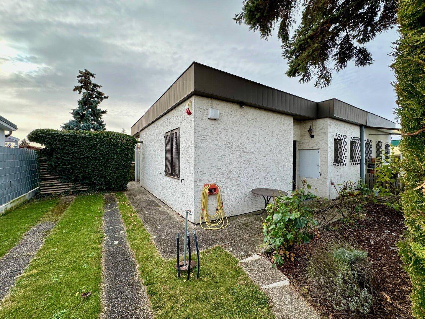 Seitenansicht des Hauses mit weißer Putzfassade, Fensterläden und einem schmalen Gartenweg.