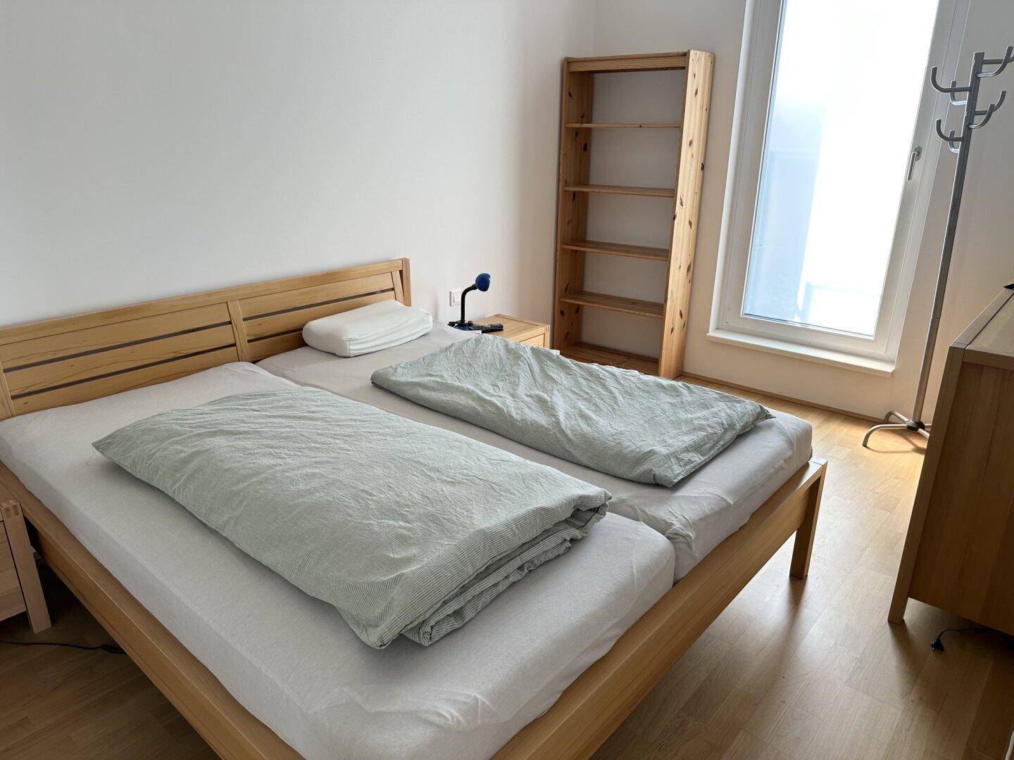 Helles Schlafzimmer mit zwei Einzelbetten, Holzrahmen und einem Bücherregal.