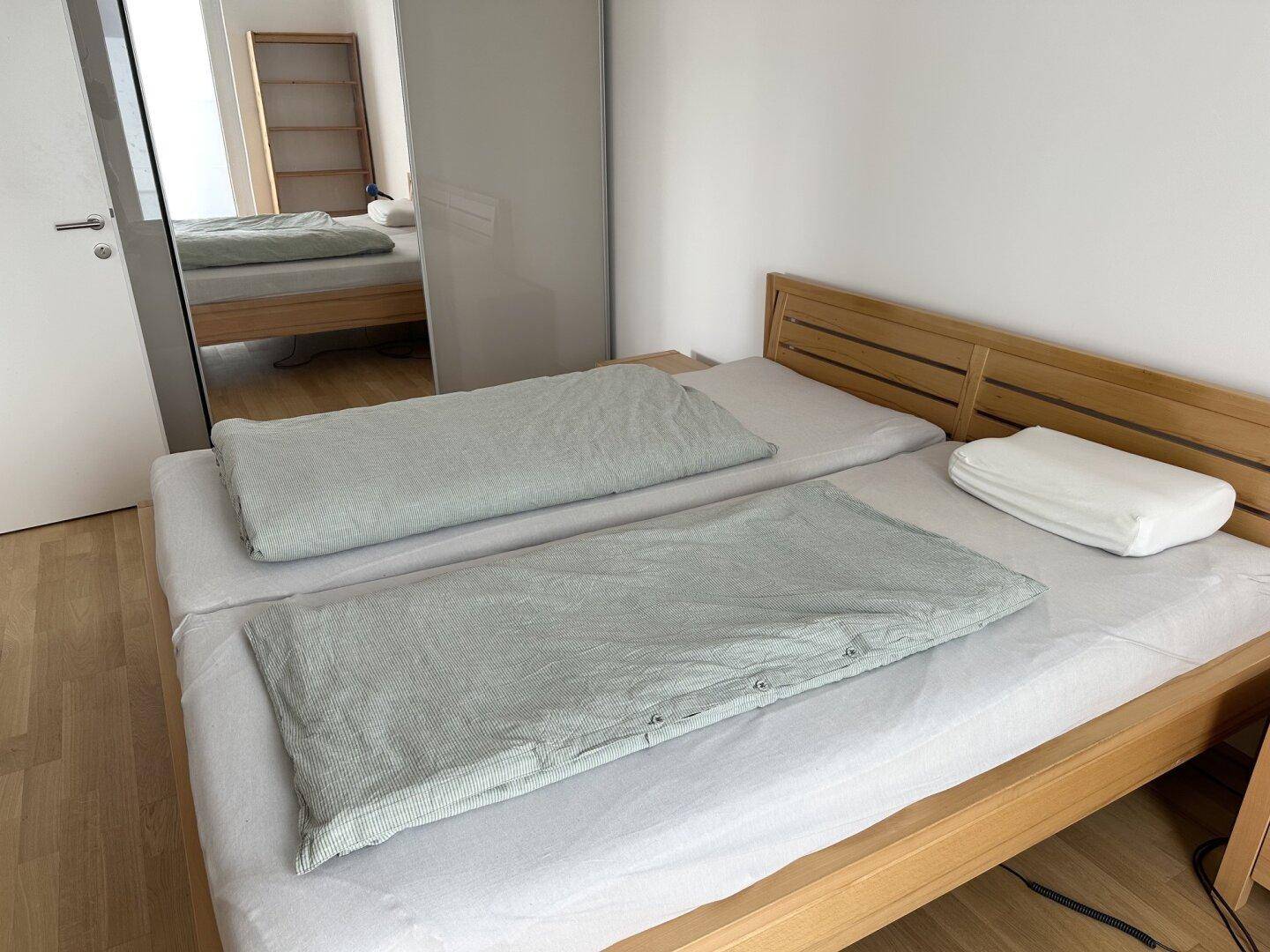 Schlafzimmer mit Holzbett, hellem Boden und einem großen Spiegelschrank.