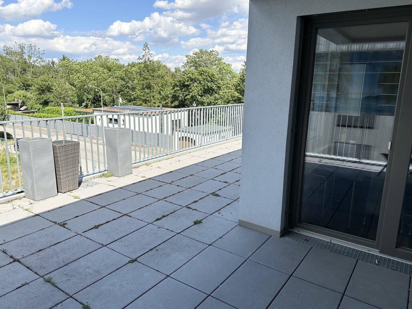 Teil der Dachterrasse mit grauen Fliesen, Pflanzenkübeln und Blick ins Grüne.