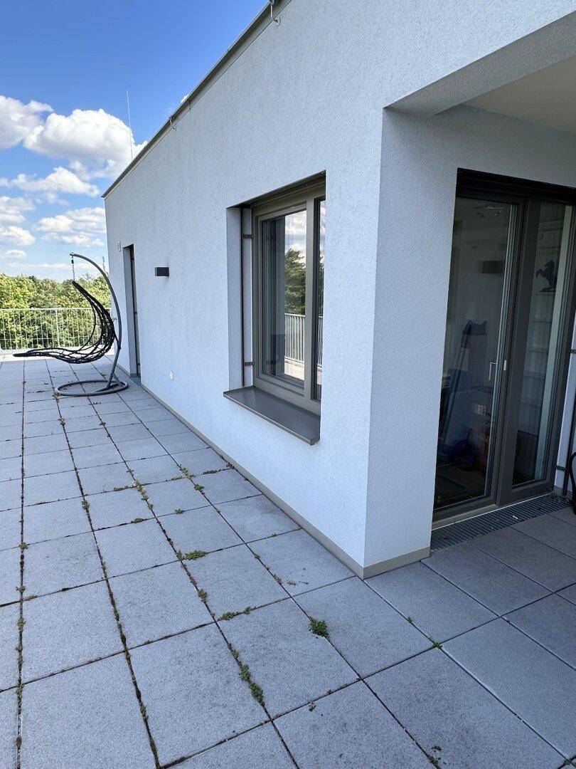 Weitläufige Dachterrasse mit grauen Fliesen, einem Hängesessel und viel Sonnenlicht.