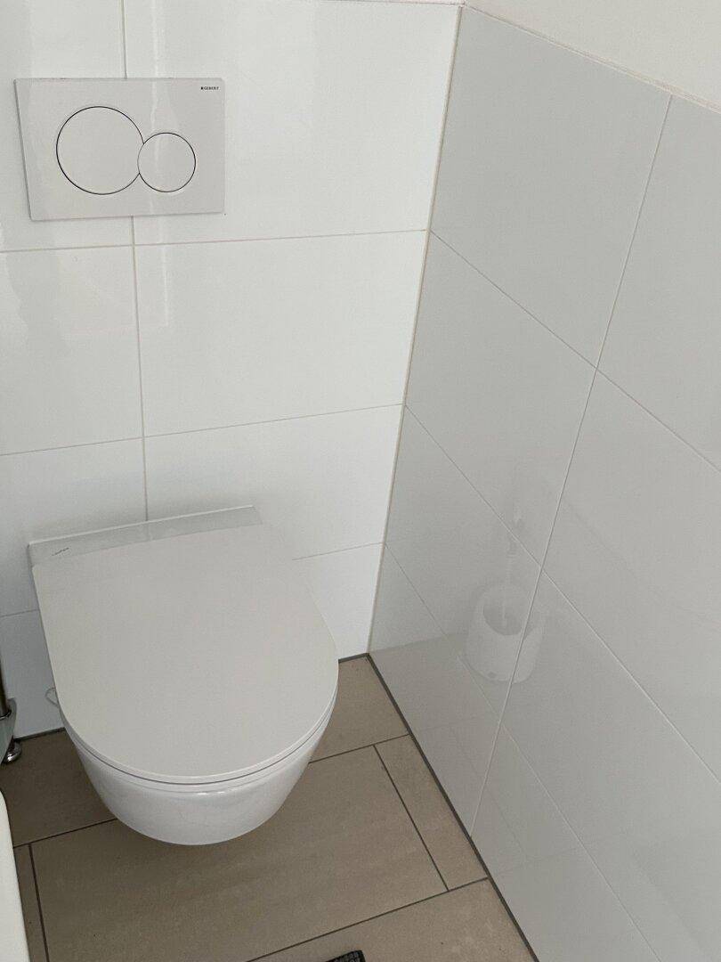 Modernes separates WC mit wandhängender Toilette und glänzenden weißen Fliesen.