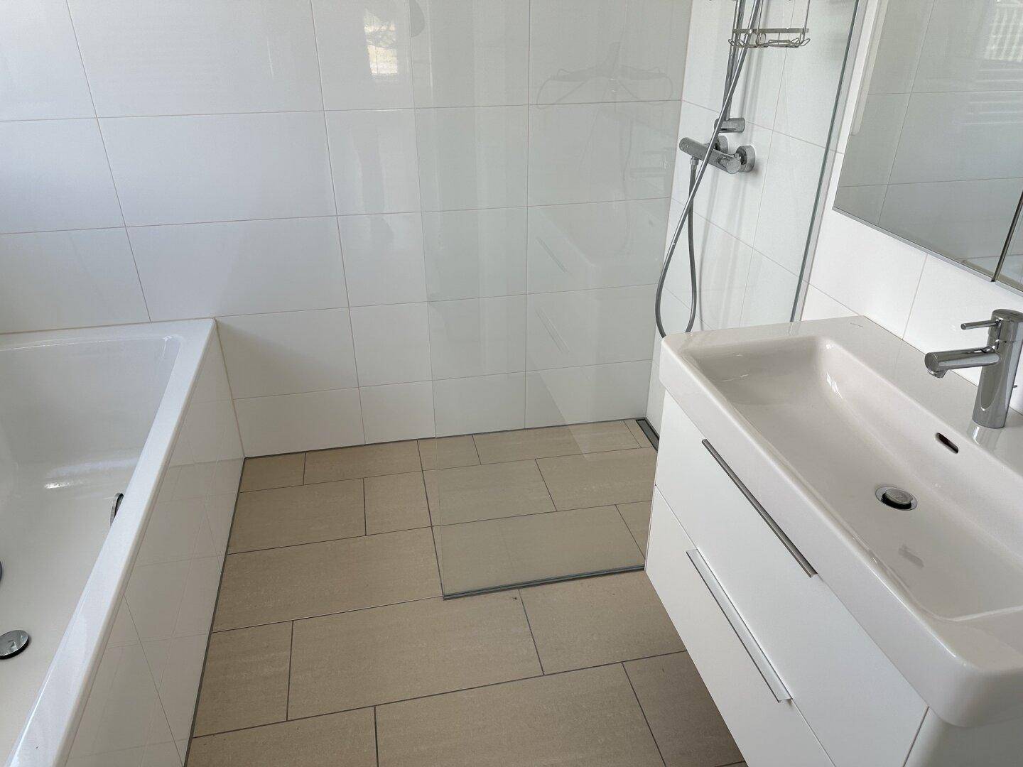 Helles Badezimmer mit Badewanne, Duschbereich und modernem Waschtisch.