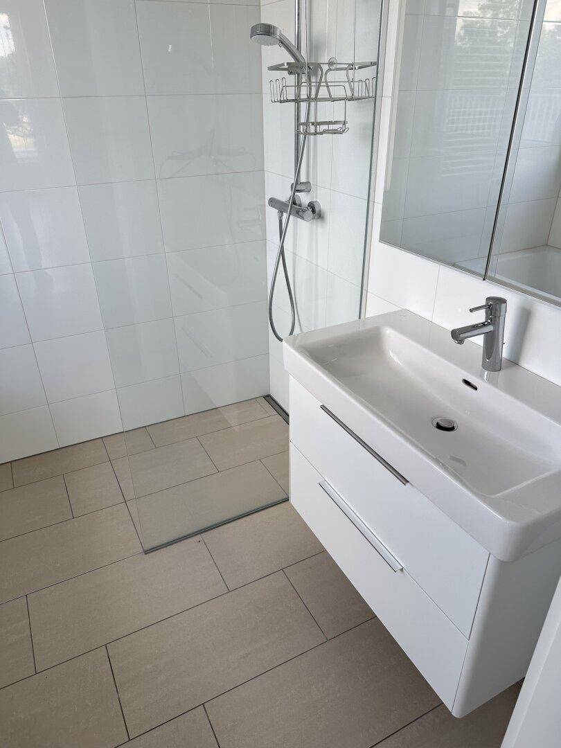 Modernes Badezimmer mit begehbarer Dusche, elegantem Waschtisch und hellen Fliesen.
