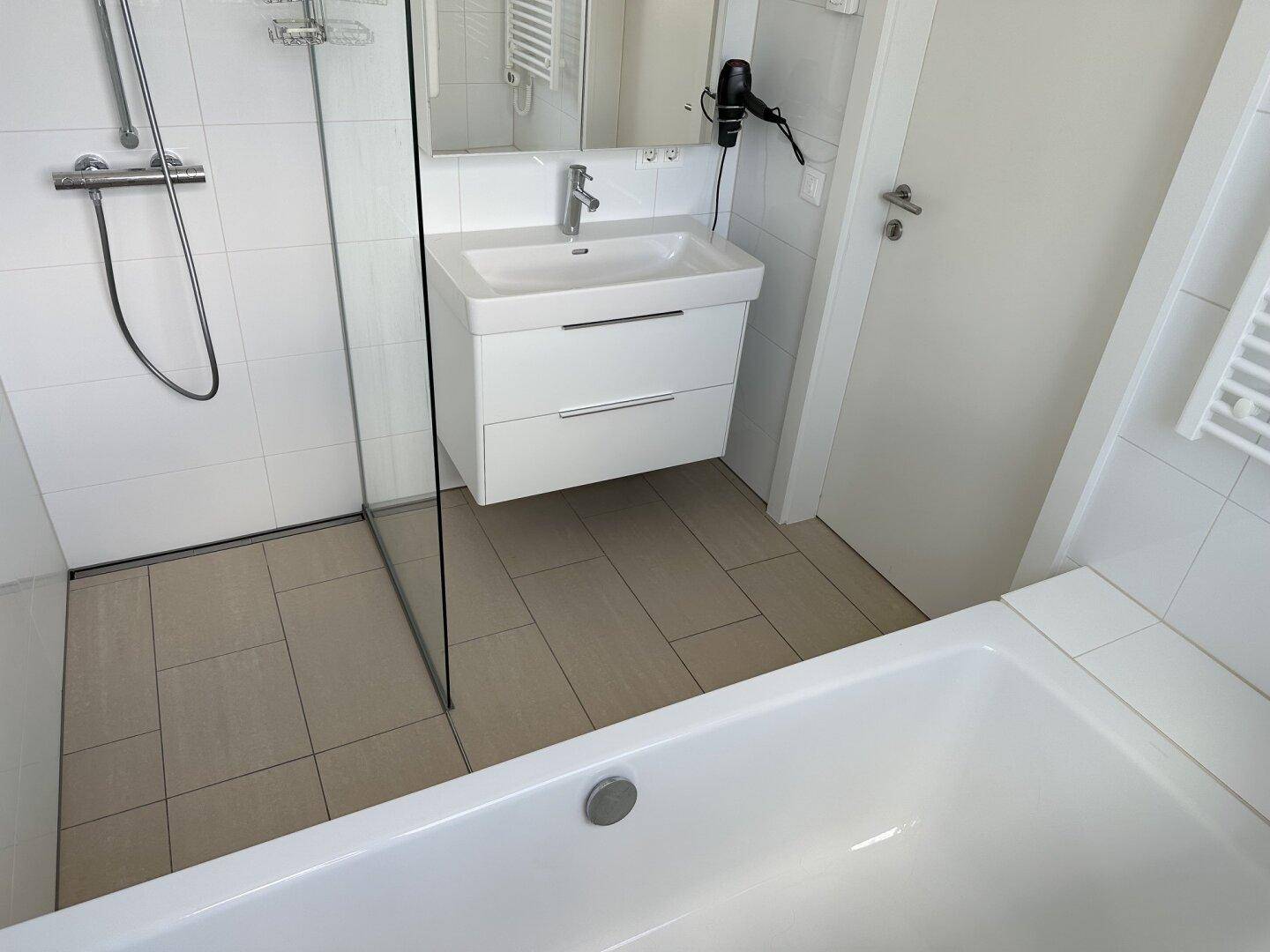 Geräumiges Badezimmer mit Badewanne, Glasduschwand und beheiztem Handtuchhalter.