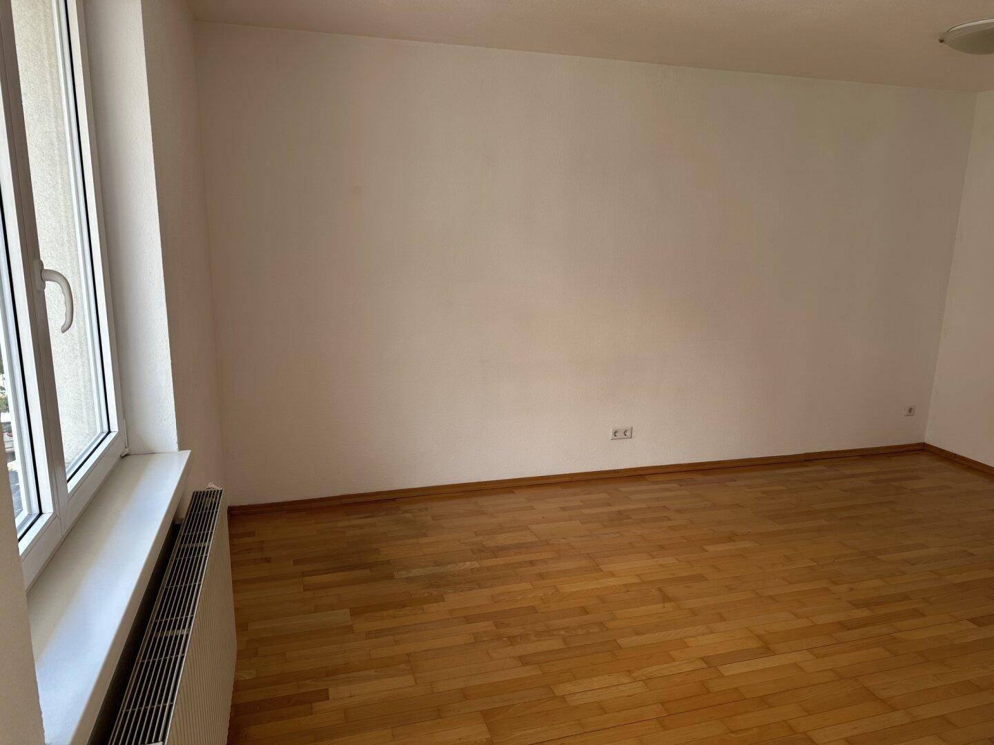Leerer Raum mit weißen Wänden und glänzendem Holzboden, bereit zur individuellen Gestaltung.