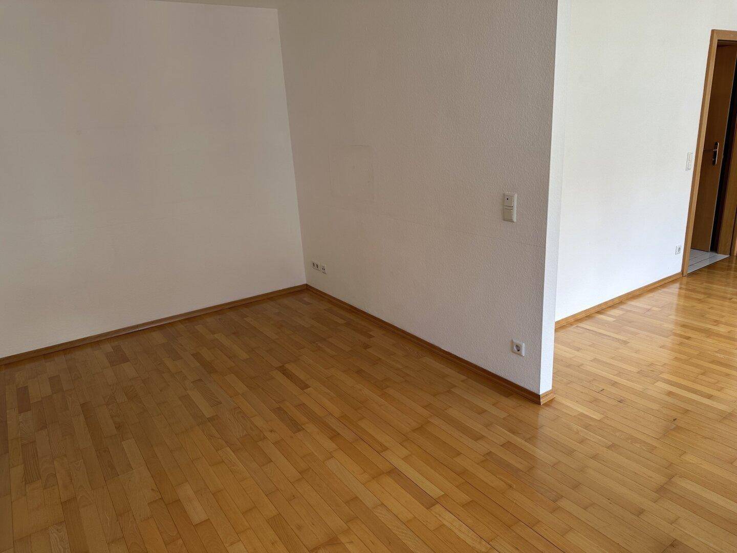 Leerer Wohnbereich mit hellen Wänden und glänzendem Parkettboden, bereit zur Einrichtung.