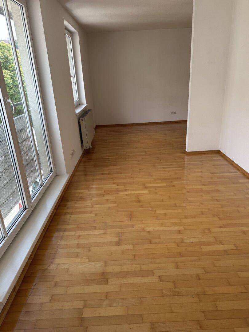 Heller Wohnbereich mit Parkettboden und großen Fenstern, die viel Tageslicht hereinlassen.