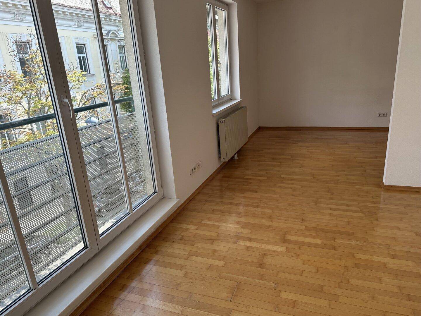Geräumiges Wohnzimmer mit Holzboden und Blick auf die umliegenden Gebäude und Bäume.