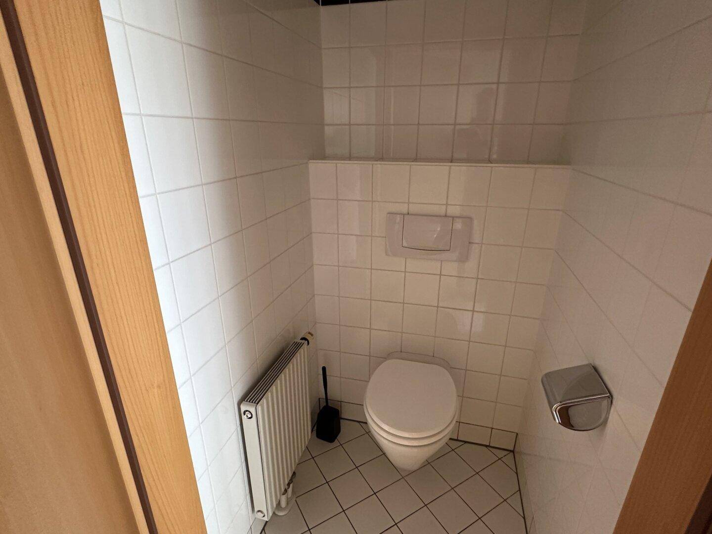 Separate Toilette mit weißen Fliesen, Wand-WC und Heizkörper, praktisch und funktional.