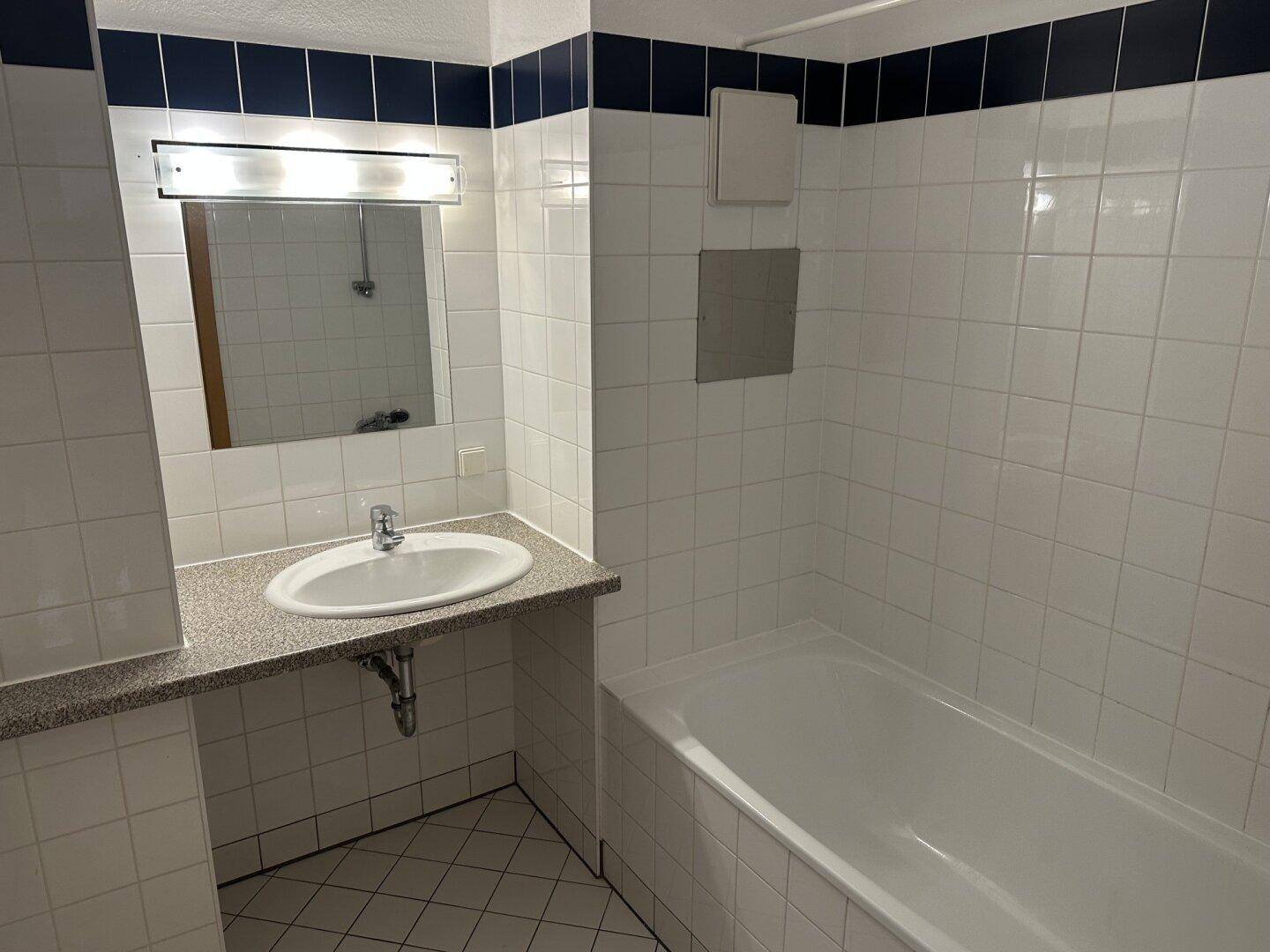 Badezimmer mit Badewanne, Waschbecken und weißen Fliesen, akzentuiert durch eine blaue Bordüre.