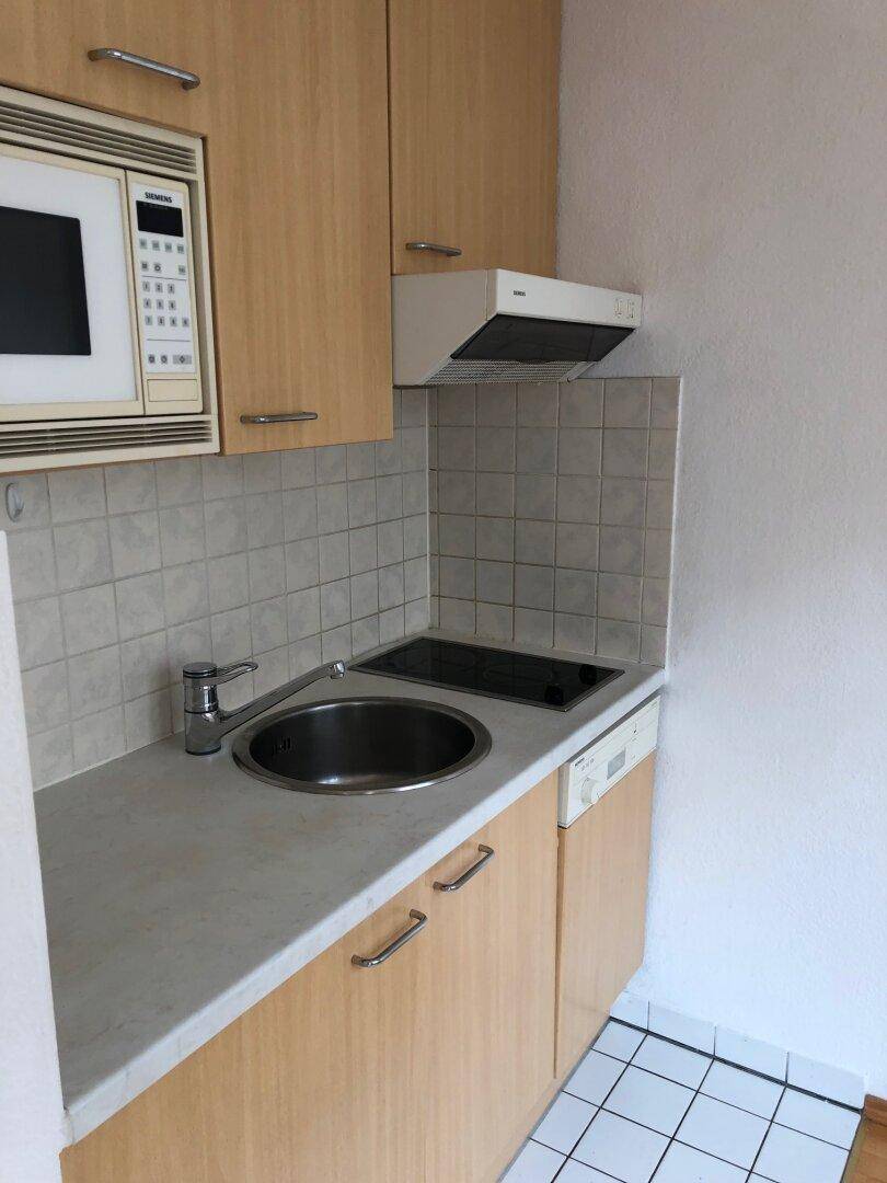 Funktionale Kochnische mit hellen Holzfronten, Spülbecken und integrierten Geräten.