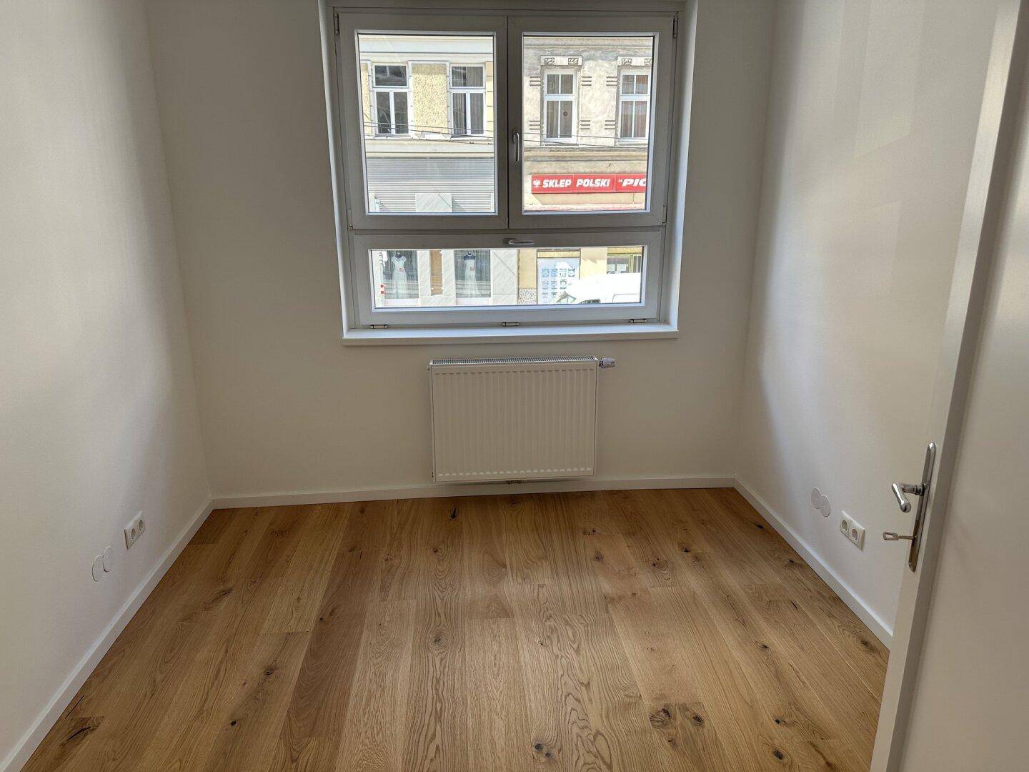 Helles Zimmer mit Holzboden und großem Fenster, das einen Blick auf die Straße bietet.