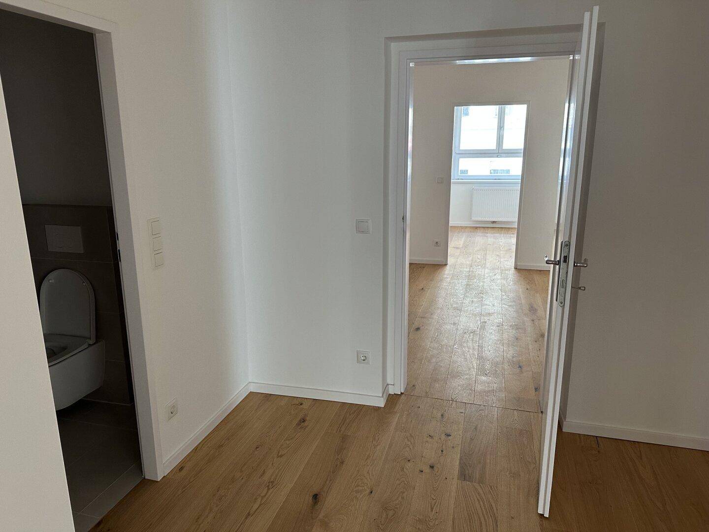 Heller Flur mit Holzboden und Zugang zu mehreren Zimmern, inklusive eines separaten WCs.