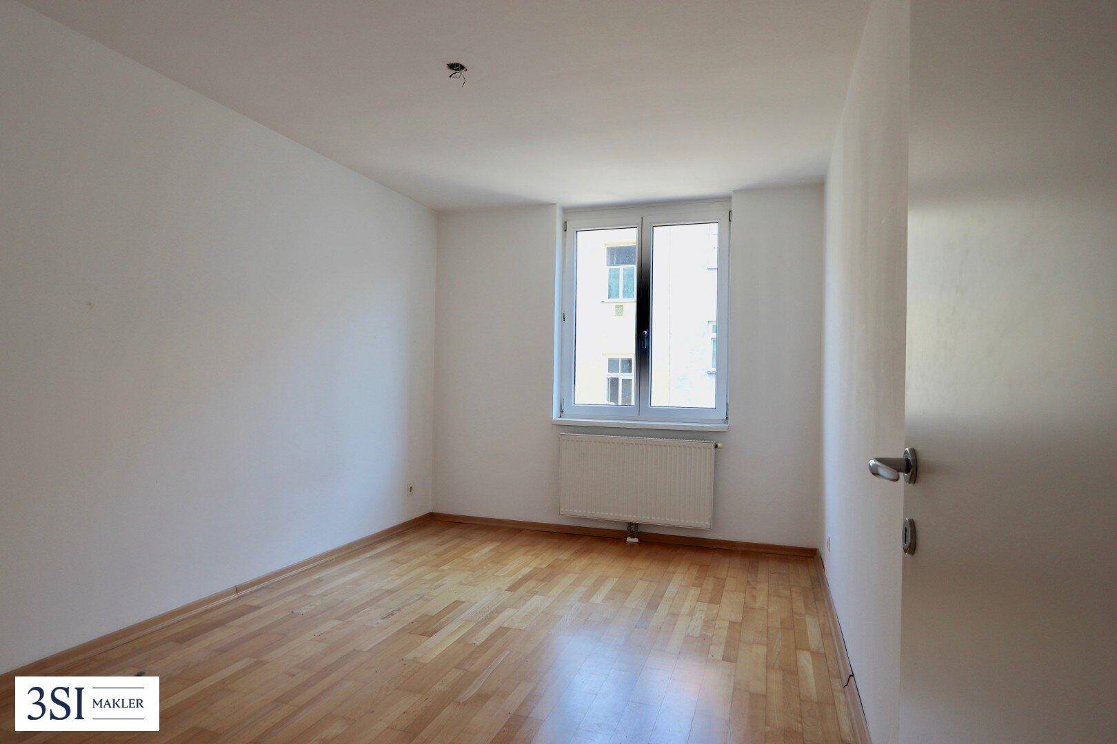 Helles, leeres Zimmer mit Holzparkett und einem Fenster, ideal als Schlaf- oder Arbeitszimmer.