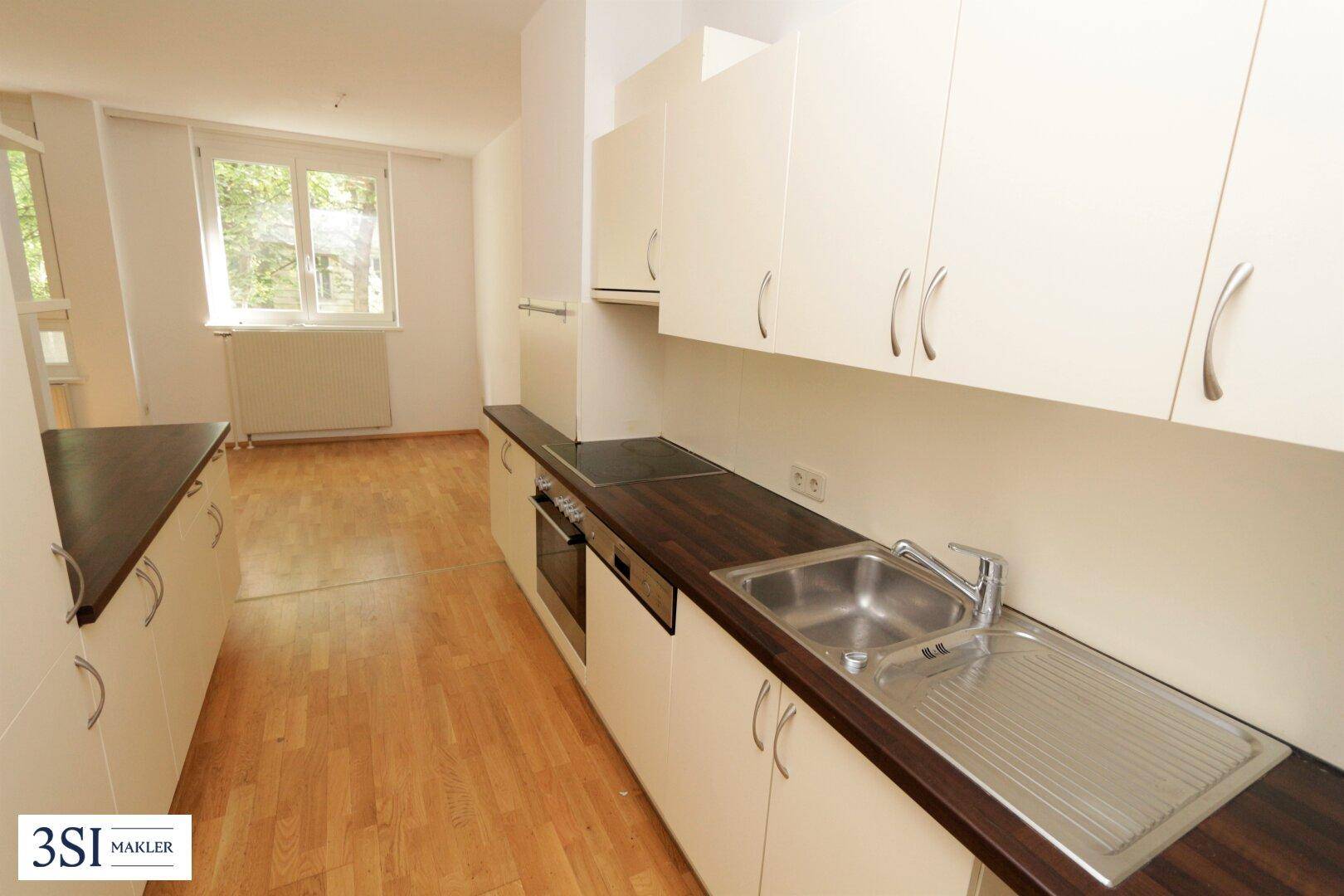 Funktionale Küche mit hellen Schränken, dunklen Arbeitsplatten und integrierten Geräten, mit Fenster.