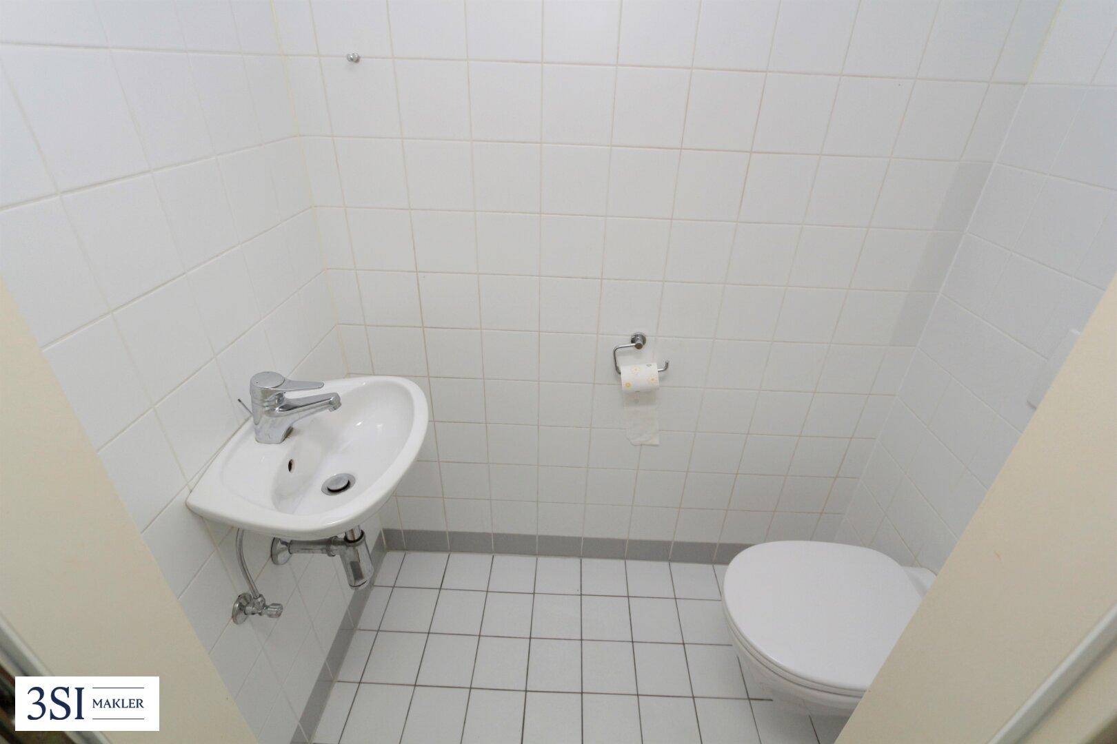 Kompaktes Gäste-WC mit weißen Fliesen, Toilette und kleinem Waschbecken, funktional gestaltet.