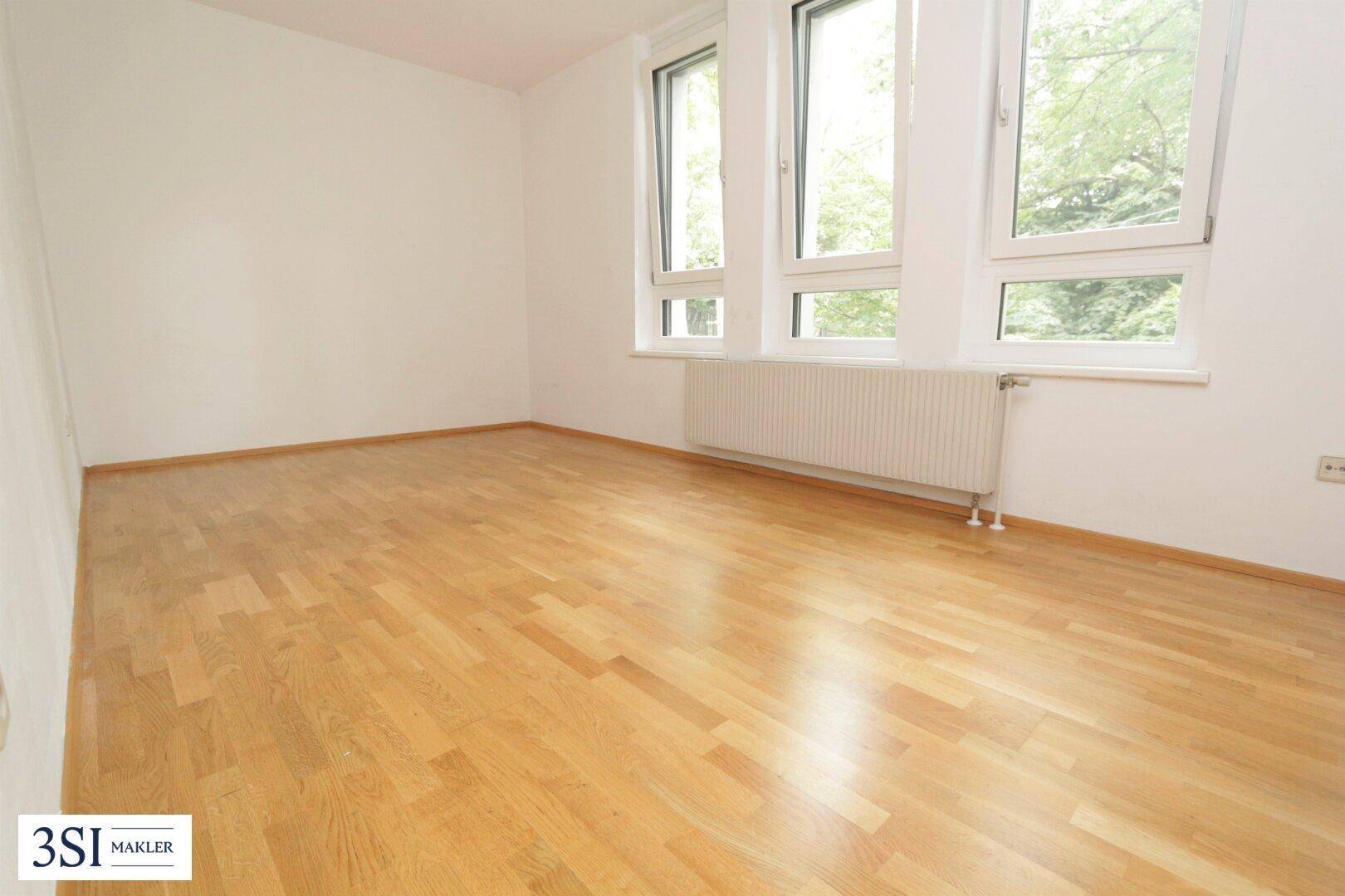 Helles Schlafzimmer mit Parkettboden, weißen Wänden und großen Fenstern mit Blick ins Grüne.