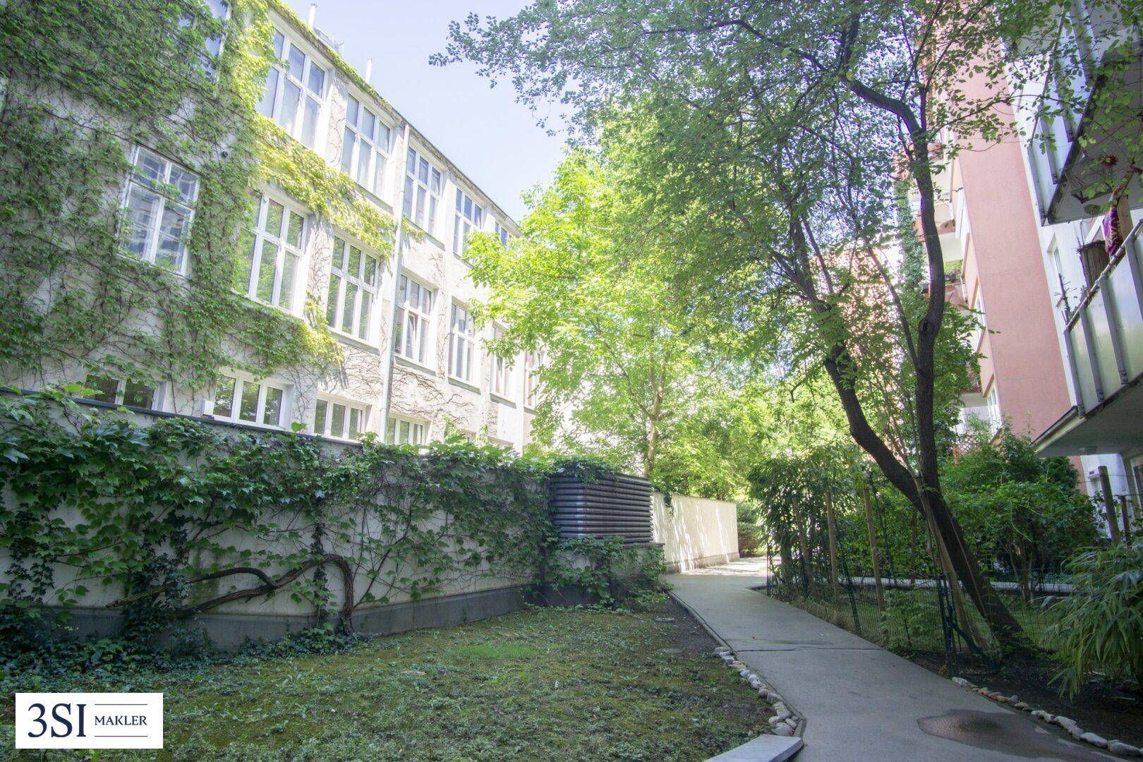 Grüner Innenhof mit bewachsenen Fassaden, Bäumen und einem Gehweg zwischen den Gebäuden.