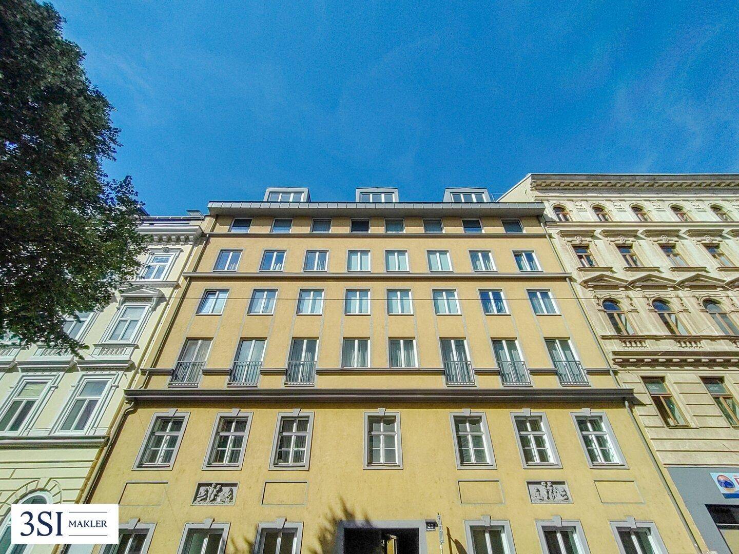 Fassade eines mehrstöckigen Wohngebäudes mit gelbem Anstrich, vielen Fenstern und französischen Balkonen.