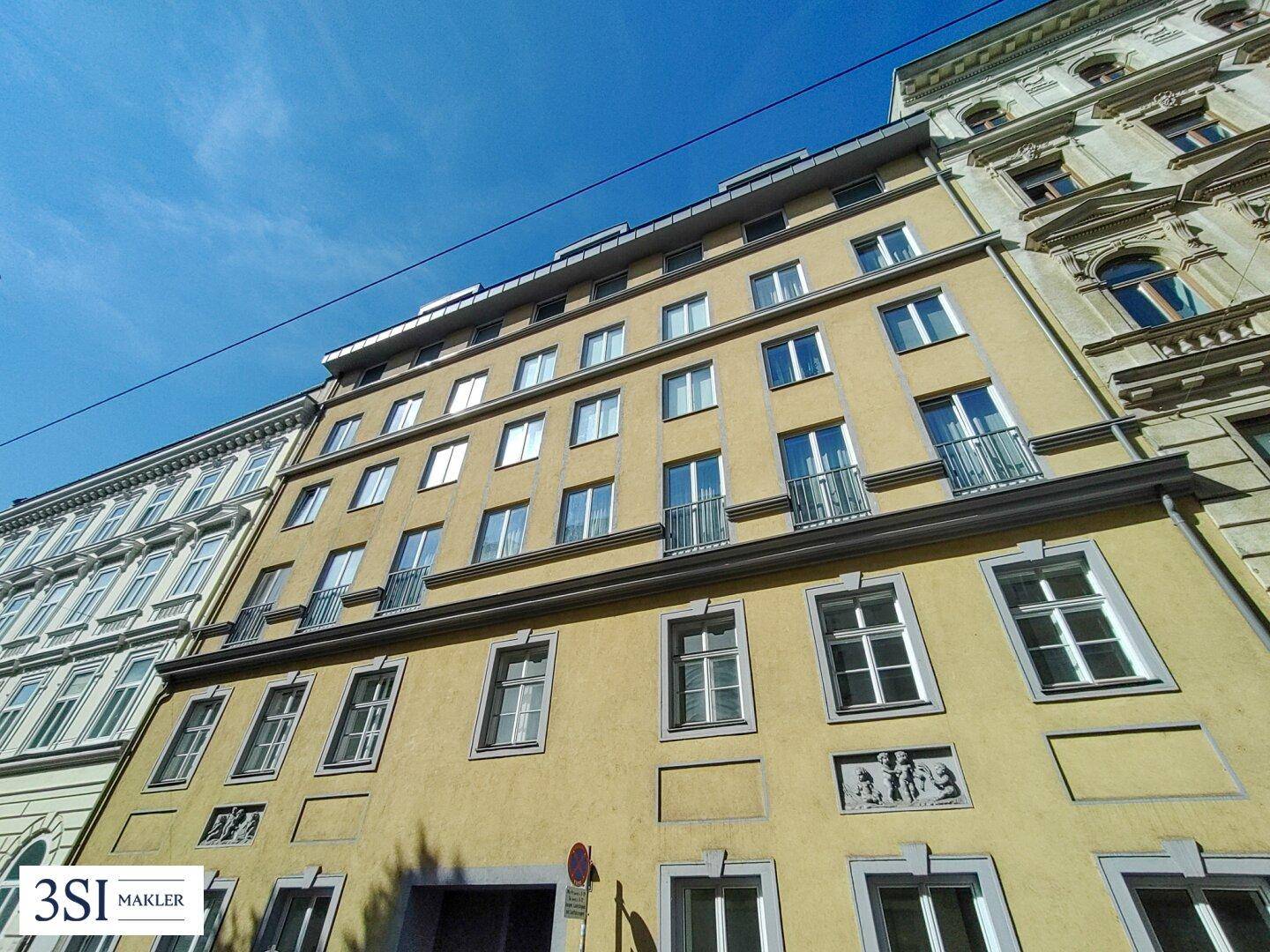 Historische Fassade eines Mehrfamilienhauses mit gelbem Anstrich und kleinen Balkonen unter blauem Himmel.