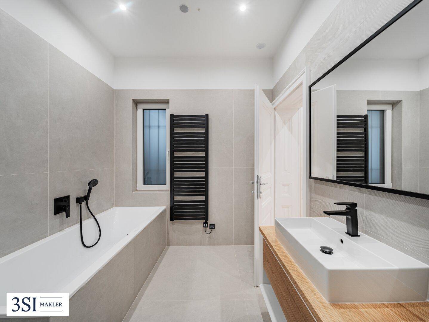 Modernes Badezimmer mit Waschtisch, Badewanne und beheiztem Handtuchhalter am Fenster.