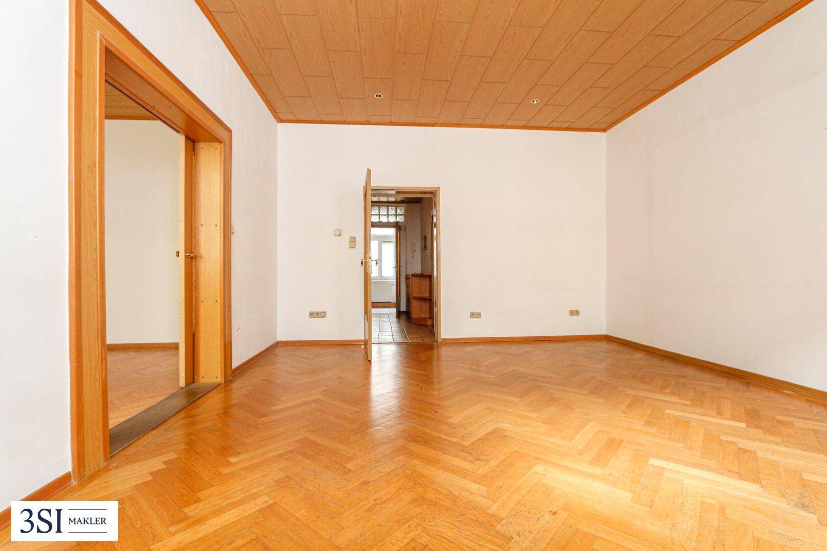 Geräumiges Wohnzimmer mit Fischgrätparkettboden und Holztäfeldecke, bereit zur individuellen Gestaltung.