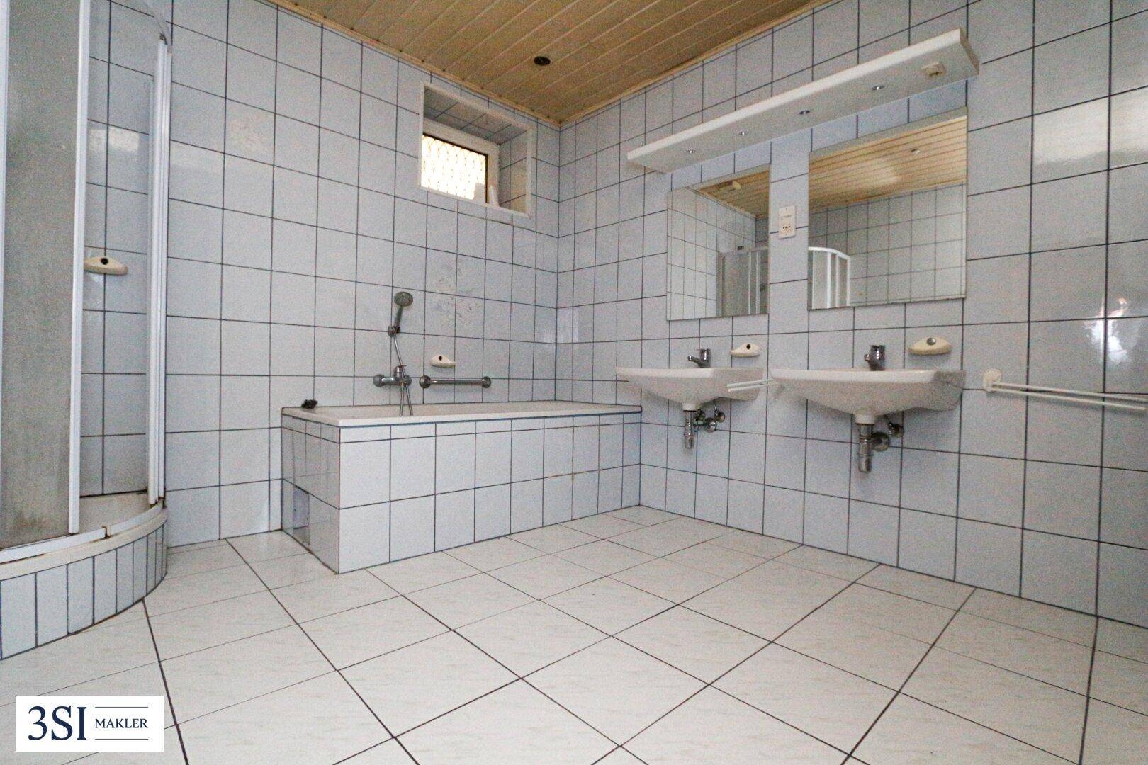 Gefliestes Badezimmer mit Badewanne, Dusche, Doppelwaschbecken und Fenster für natürliche Belüftung.