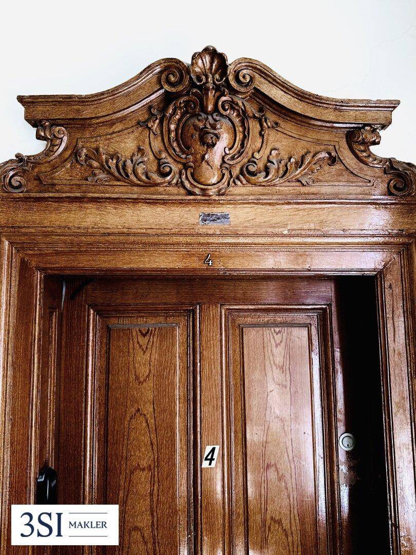 Detailaufnahme einer reich verzierten Holztür mit Schnitzereien und Hausnummer.