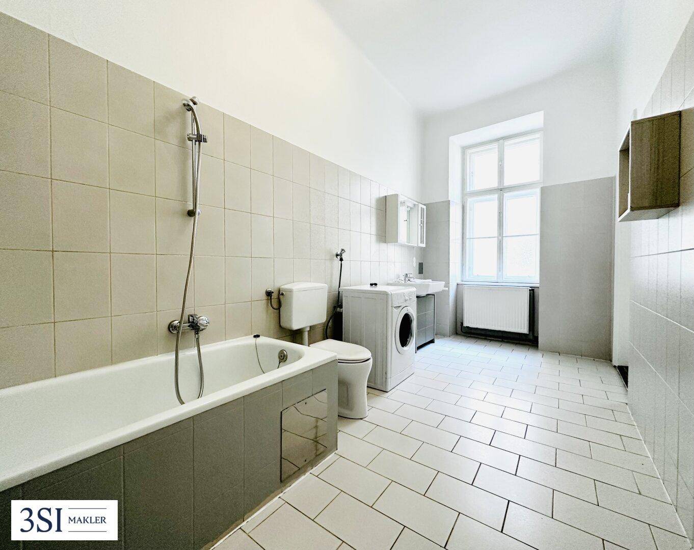Geräumiges Badezimmer mit Badewanne, Waschmaschine und Fenster für Tageslicht.