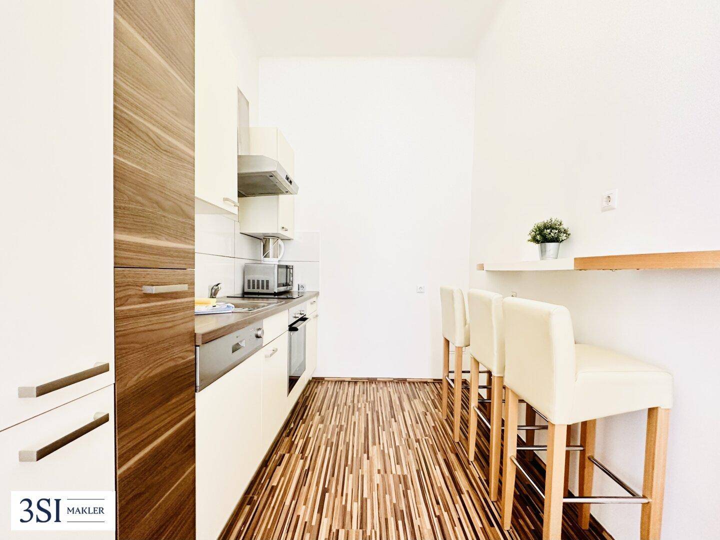 Helle, moderne Küche mit Holzboden, integrierten Geräten und einer Frühstückstheke für zwei Personen.