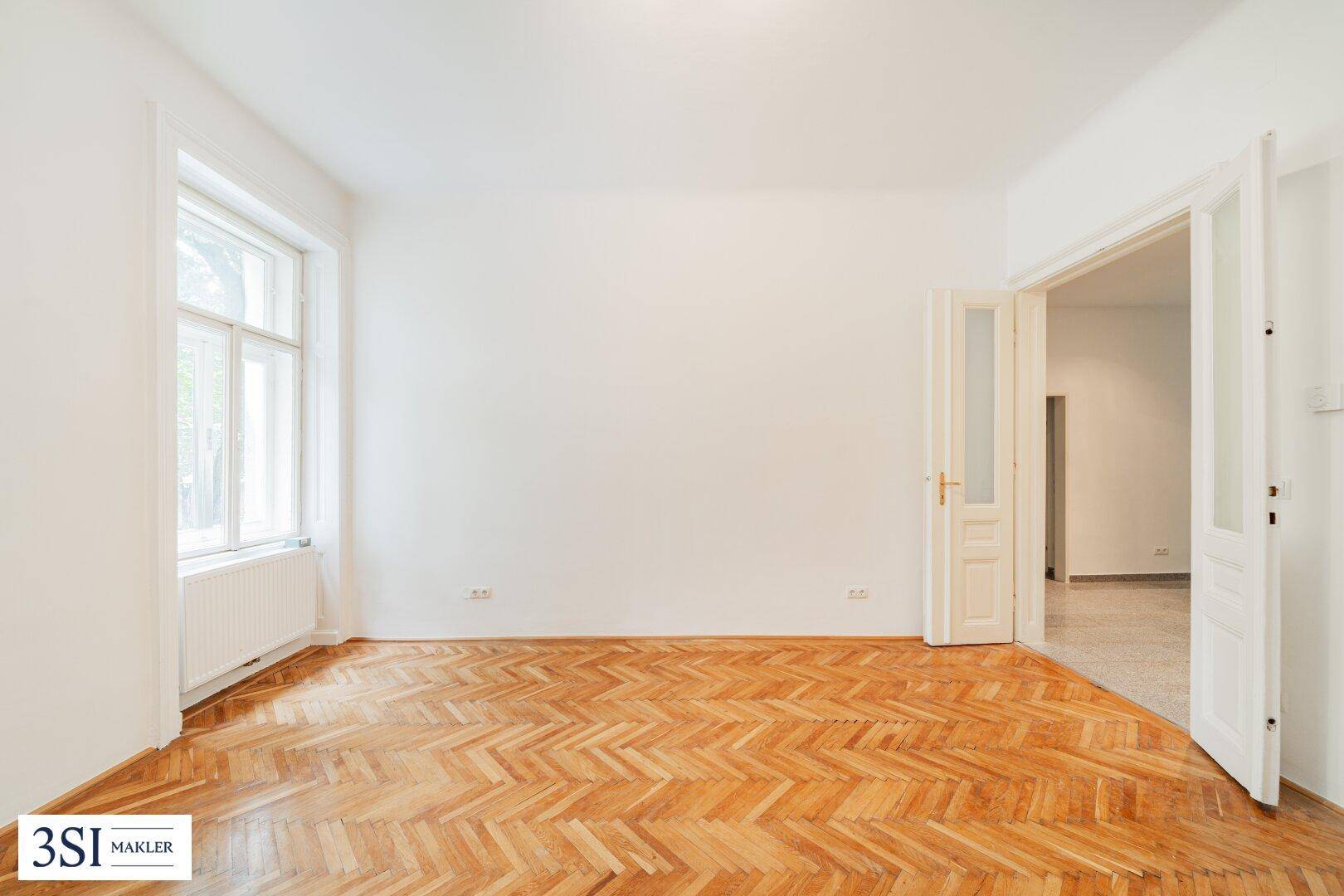 Helles Zimmer mit klassischem Fischgrätparkett und Flügeltüren zu einem weiteren Raum.