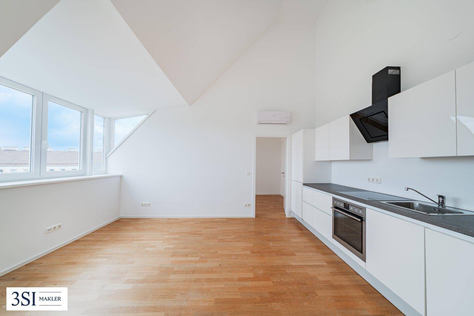 Moderne Einbauküche mit weißen Schränken, Holzboden und viel Tageslicht im Dachgeschoss.