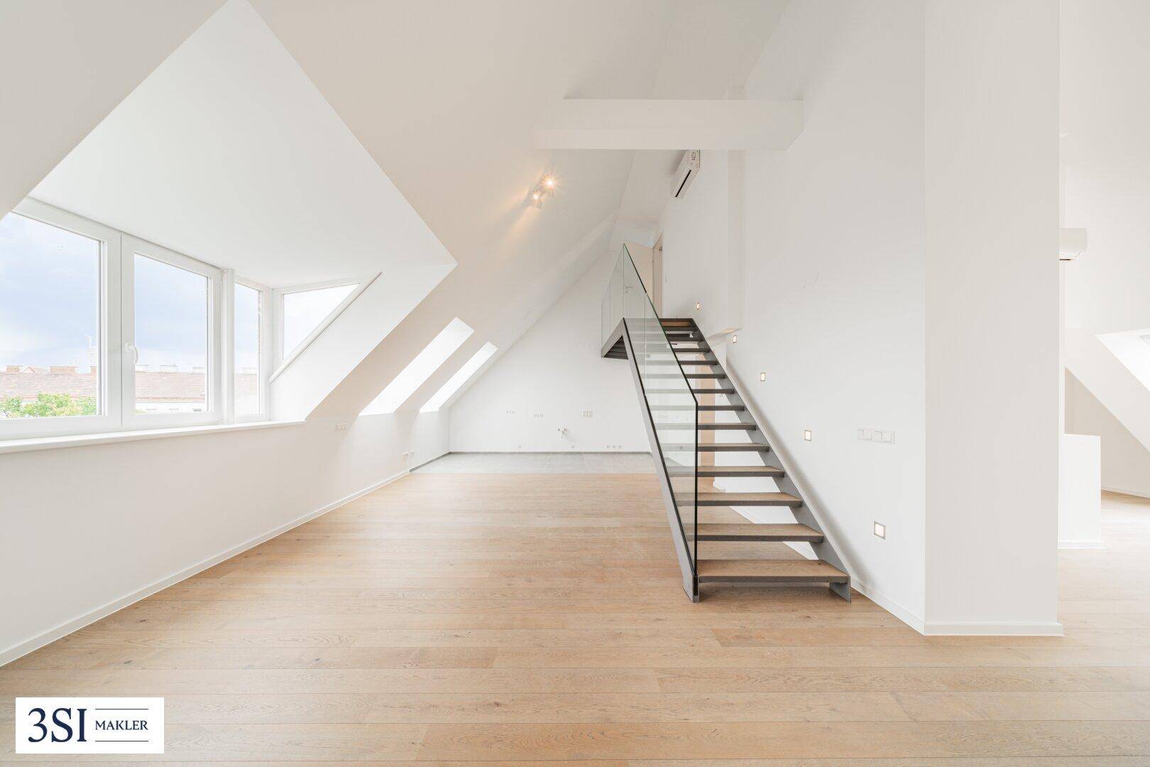 Helles Dachgeschosszimmer mit Holzboden, schrägen Wänden und moderner Treppe.